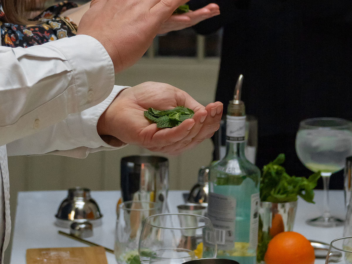 Table contenant différentes choses destinées à la préparation de cocktails : alcools, shakers, orange, menthe fraîche, doseur, mélangeur, etc.