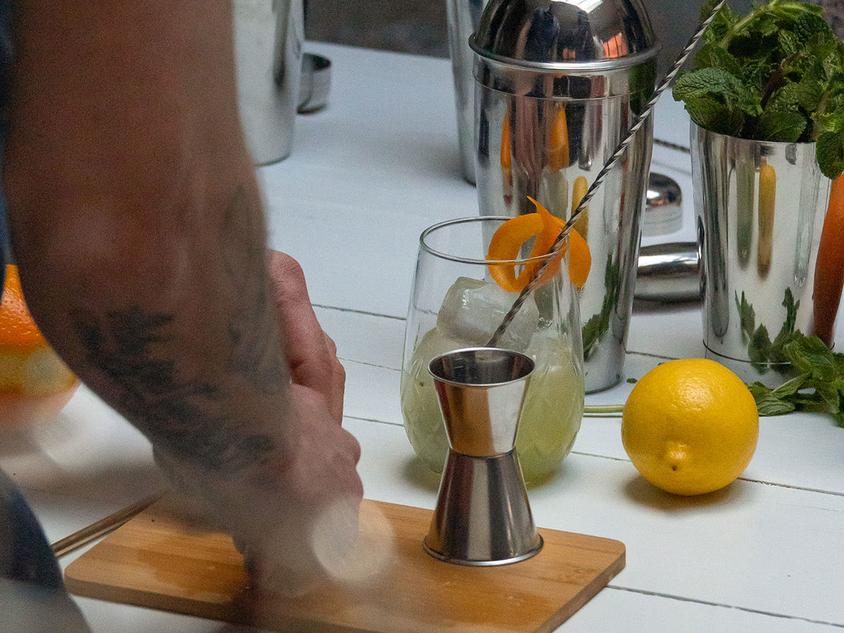 Table contenant différentes choses destinées à la préparation de cocktails : alcools, shakers, citron, menthe fraîche, doseur, mélangeur, etc.