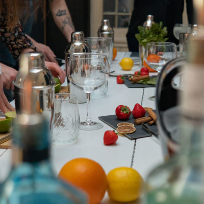 Table remplie de produits (fraises, citrons, oranges, cannelle...) et d'accessoires (verres, shakers, doseurs) pour la préparation de cocktails