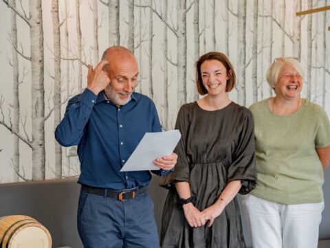 Un homme et deux femmes souriants debout en train de lire une énigme lors d'un escape game